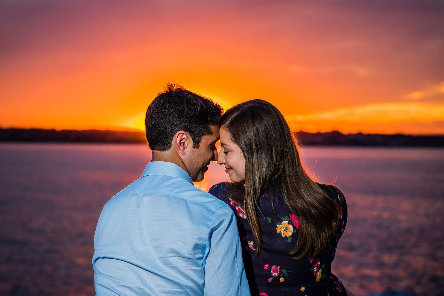 Couple silhouetted against vibrant orange sunset over calm water, photographed by a Rhode Island photographer.