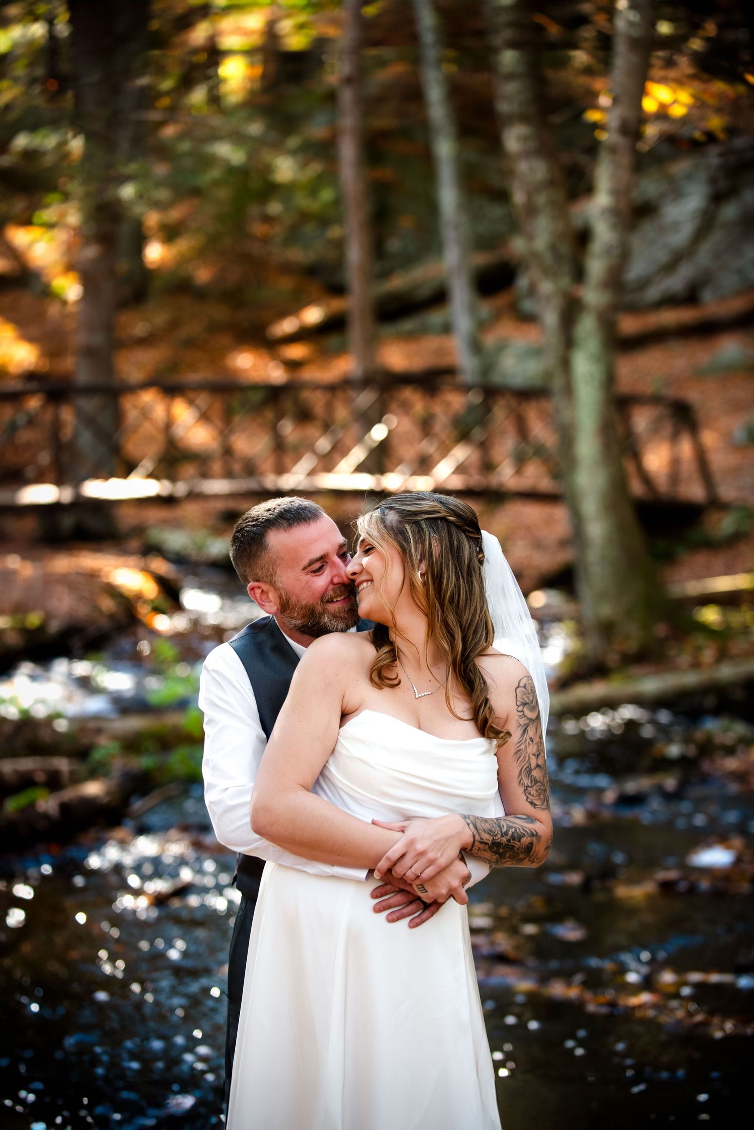 A wedding couple shares moment in a wooded setting with sunlight filtering through the trees.  Taken by Rhode Island Elopement Photographer