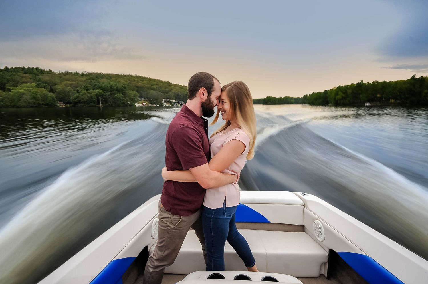Couple shares tender moment on pontoon boat during sunset on peaceful lake, photographed by a Rhode Island photographer.