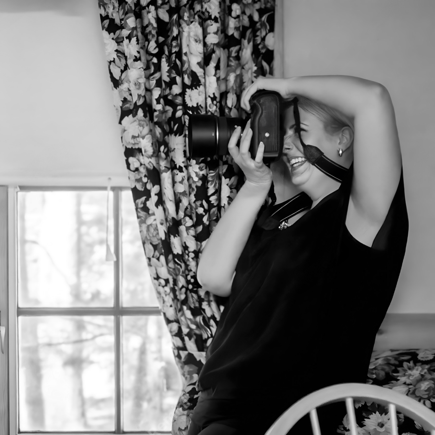 Rhode Island Photographer in black holding camera against floral curtain background in black and white.