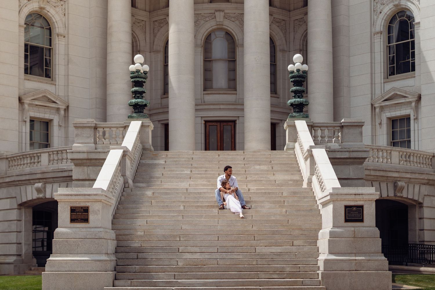 Person in white dress sitting on steps of grand neoclassical government building with ornate columns and lamp posts.