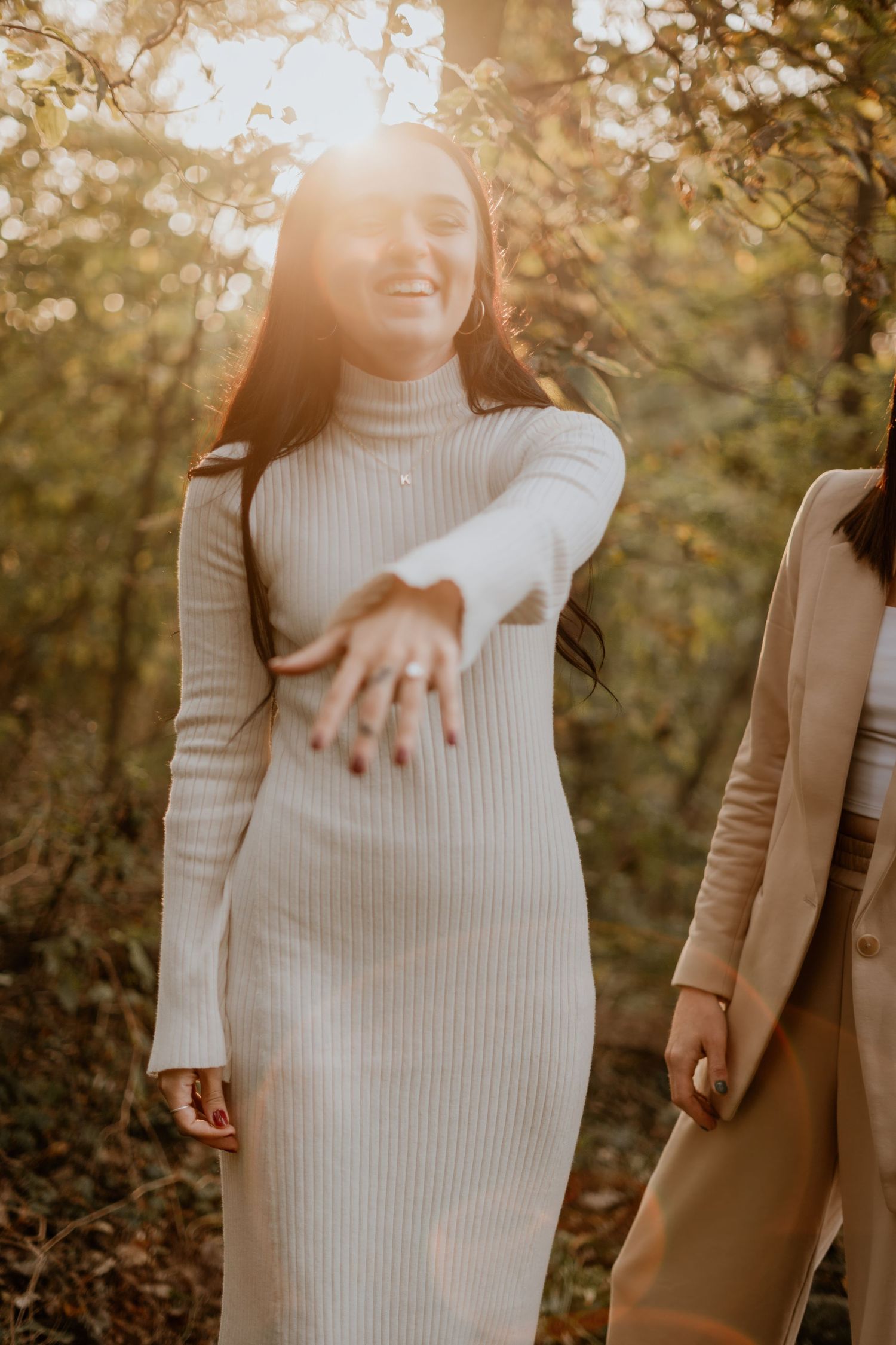 A couple in neutral tones showing off an engagement ring during a fall photoshoot.