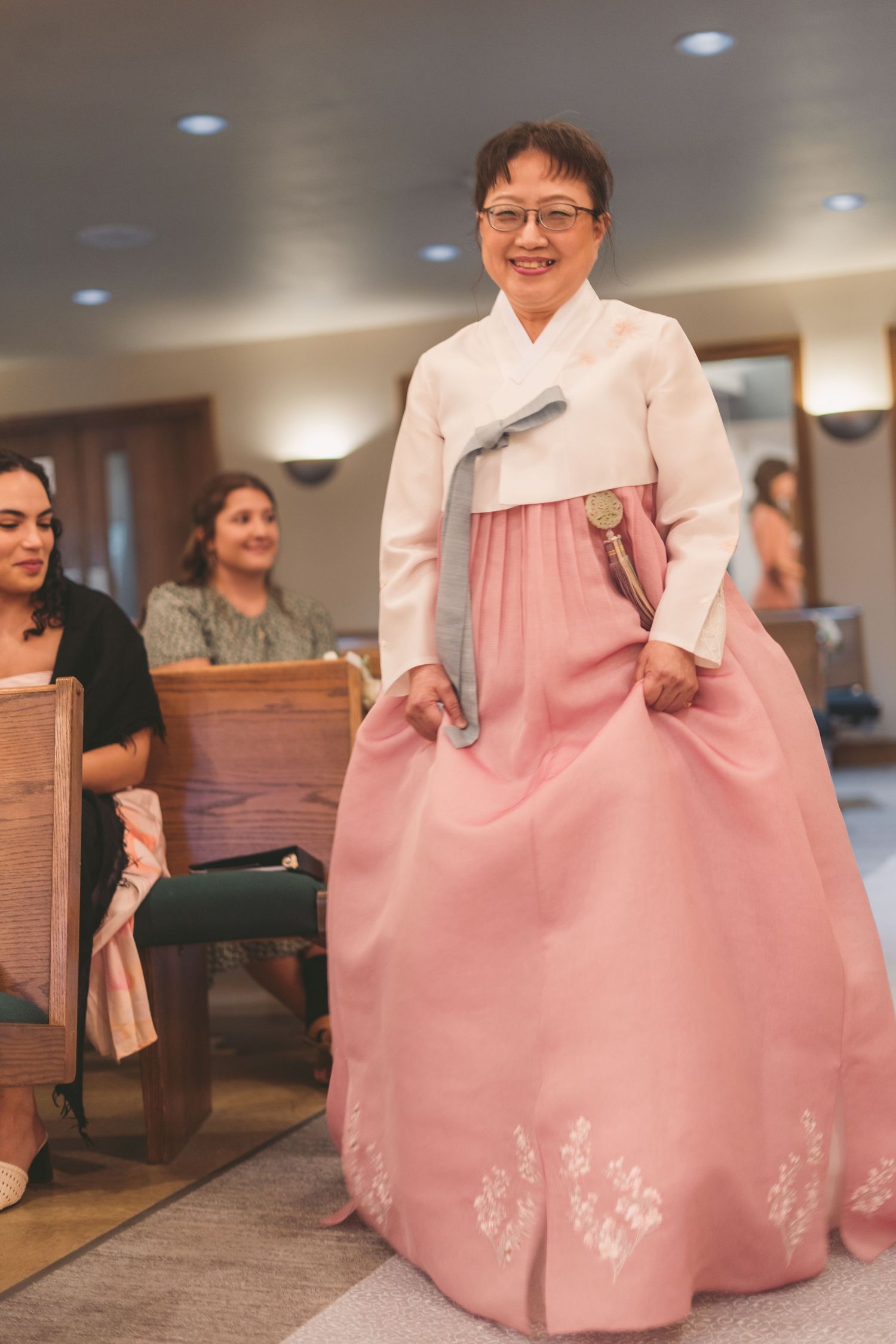 Smiling woman wearing a traditional Korean hanbok with pink skirt and white top at a formal event.