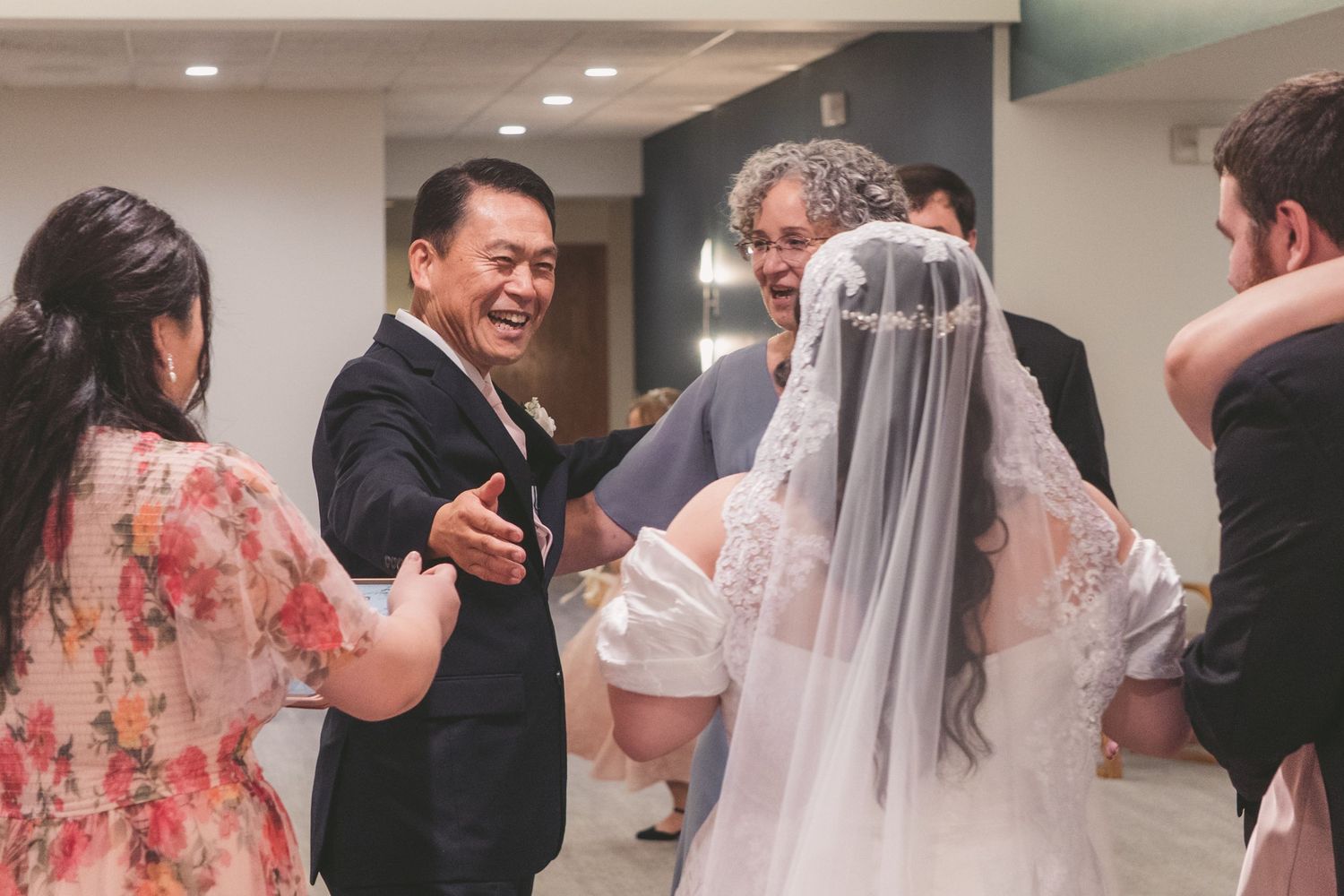Joyful wedding reception scene with guests in formal attire congratulating a bride in a white gown and veil.