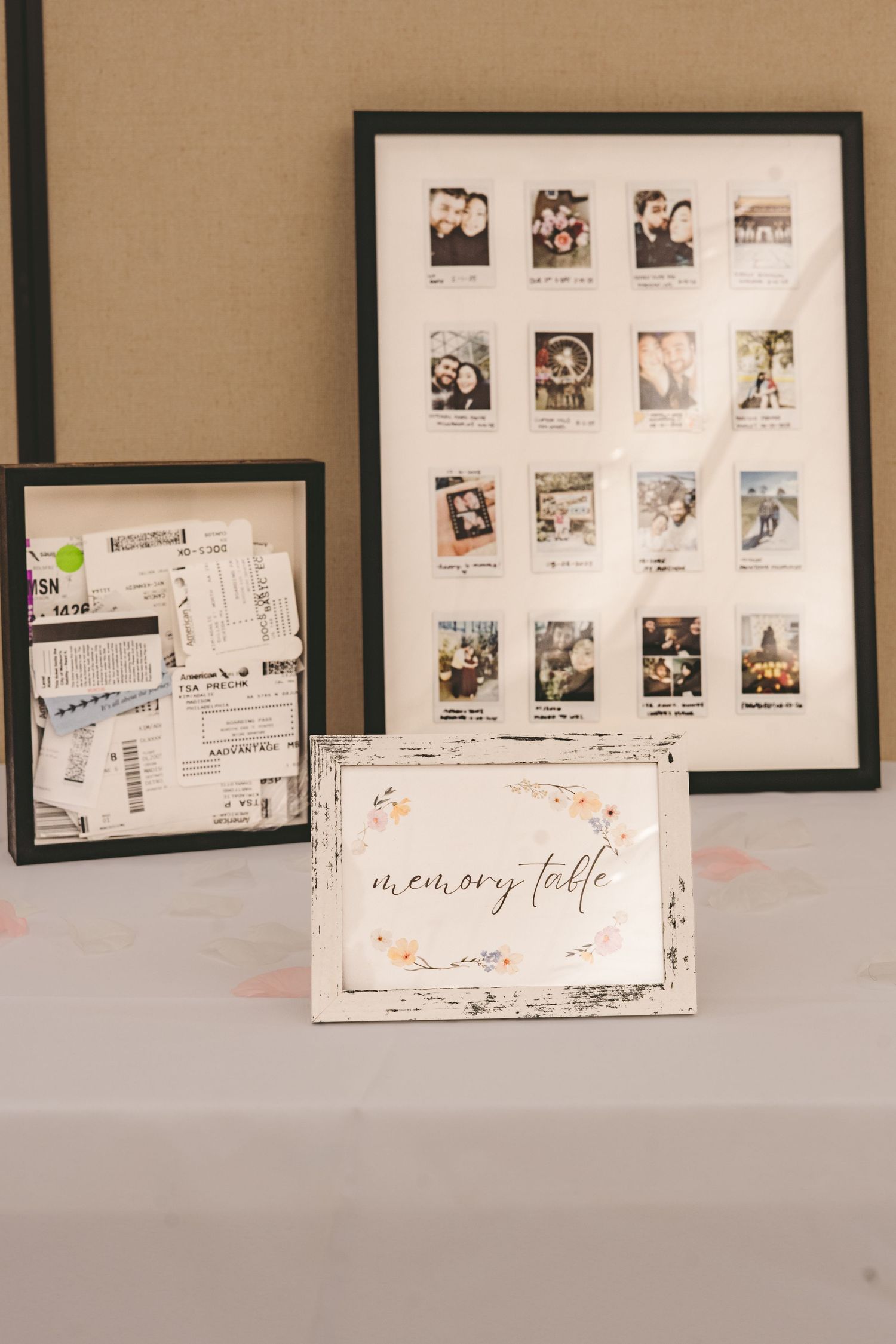 A wedding memory table display featuring a framed grid of Polaroid photos, ticket stubs, and a decorative sign.