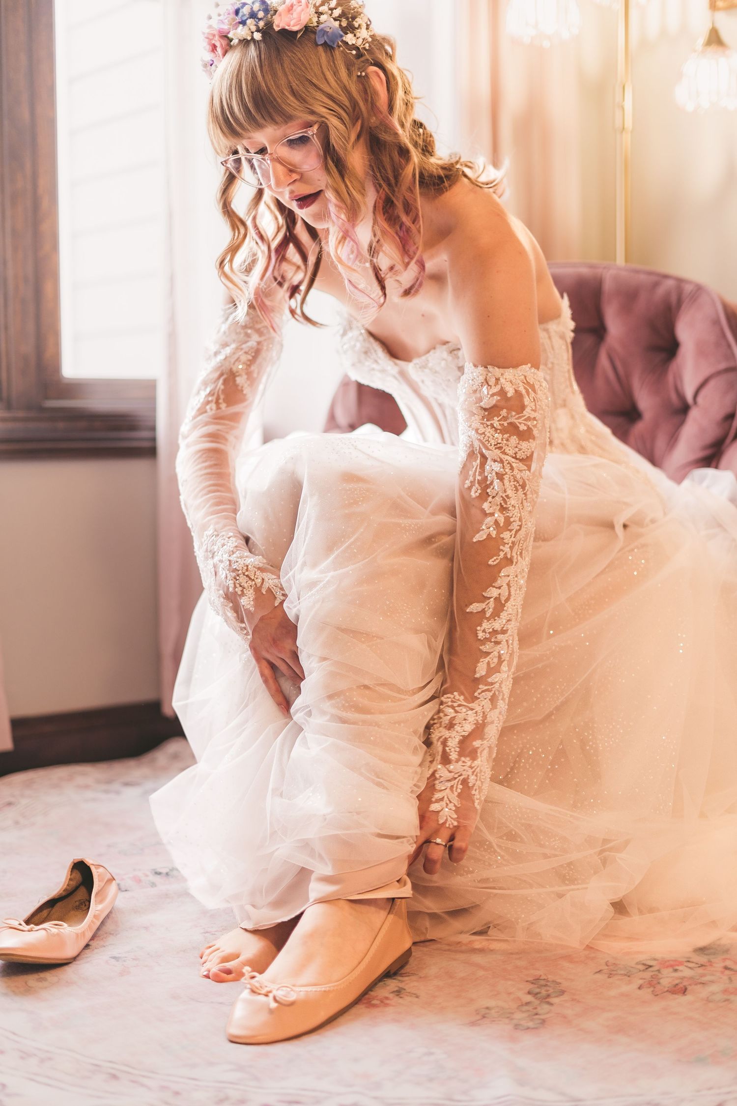 Bride in floral crown and lace gloves putting on ballet flats before her wedding ceremony.
