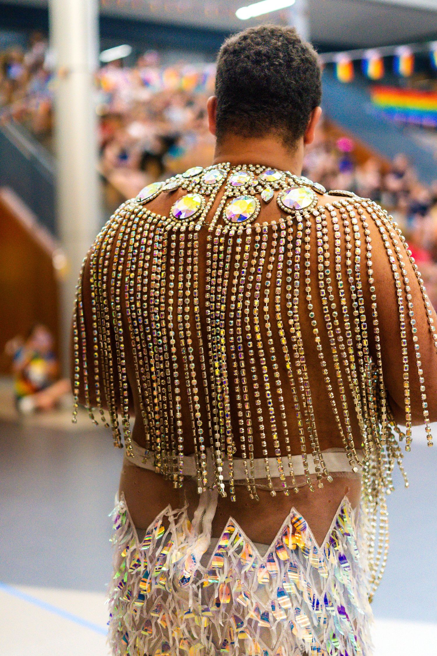 Person wearing ornate gold beaded cape with rhinestones at colorful Pride event celebration.