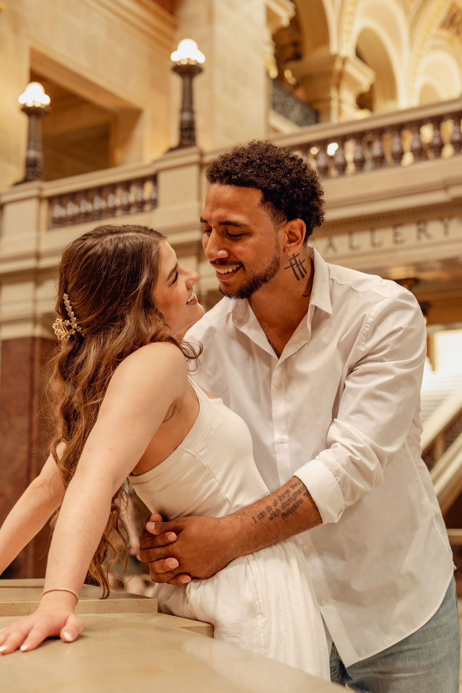 Smiling interracial couple sharing a romantic embrace inside an elegant historic building gallery.