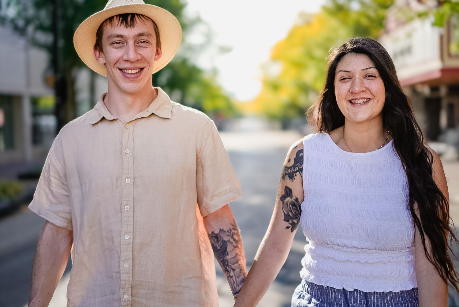 A couple enjoys a stroll down a tree-lined street on a bright summer day.