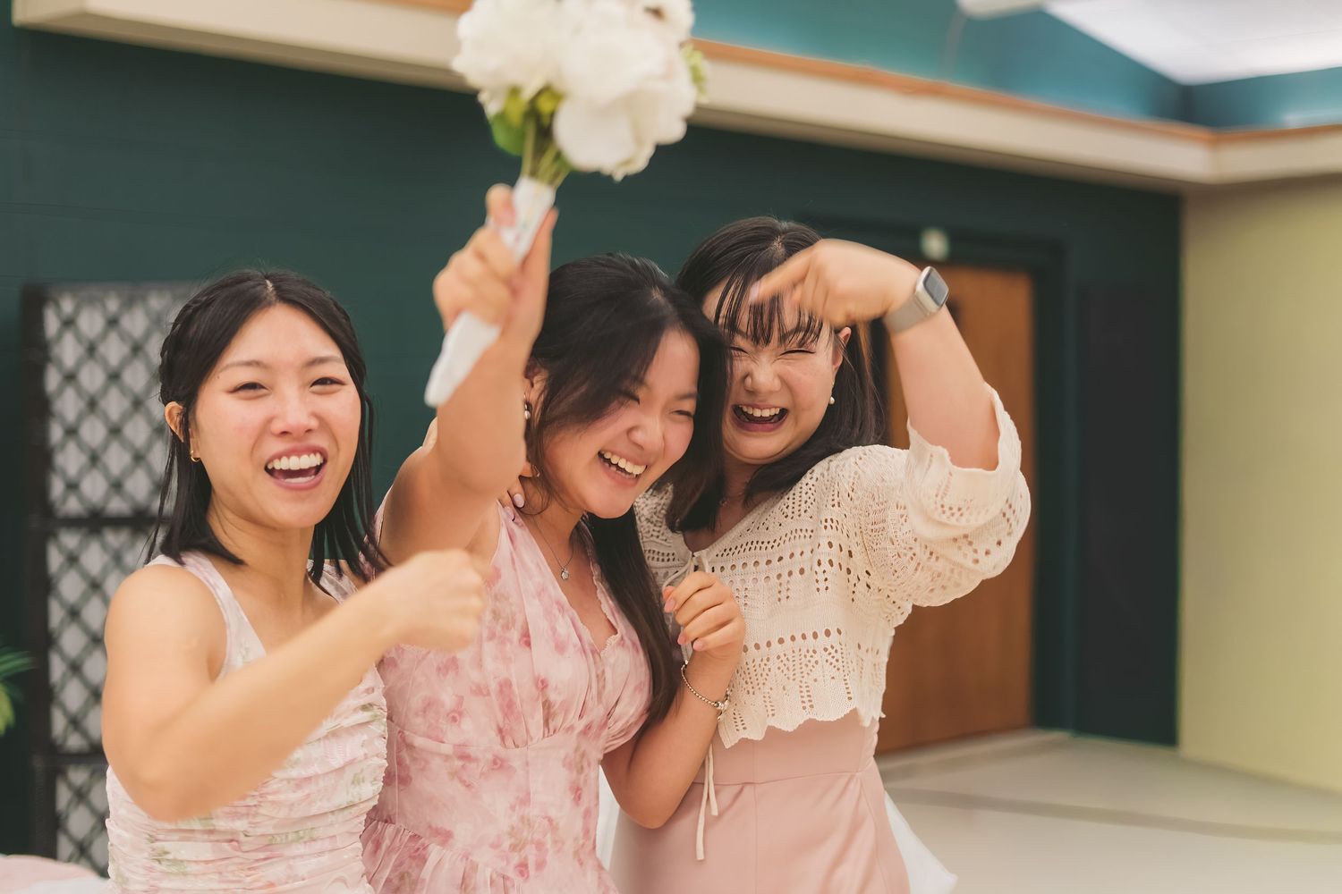 Three joyful bridesmaids celebrate with white bouquet at wedding reception outdoors.