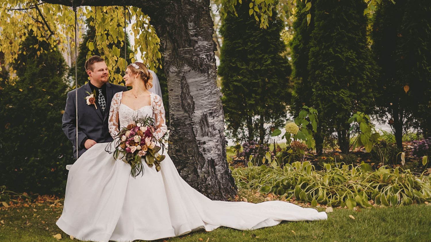 Newlyweds pose under yellow autumn trees during outdoor wedding ceremony.