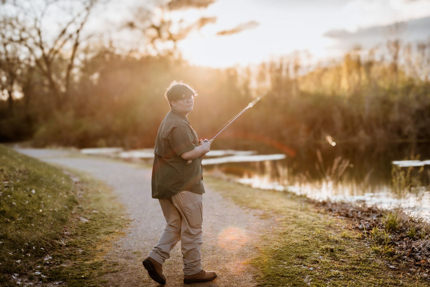 Child walking along path during sunset near a pond.