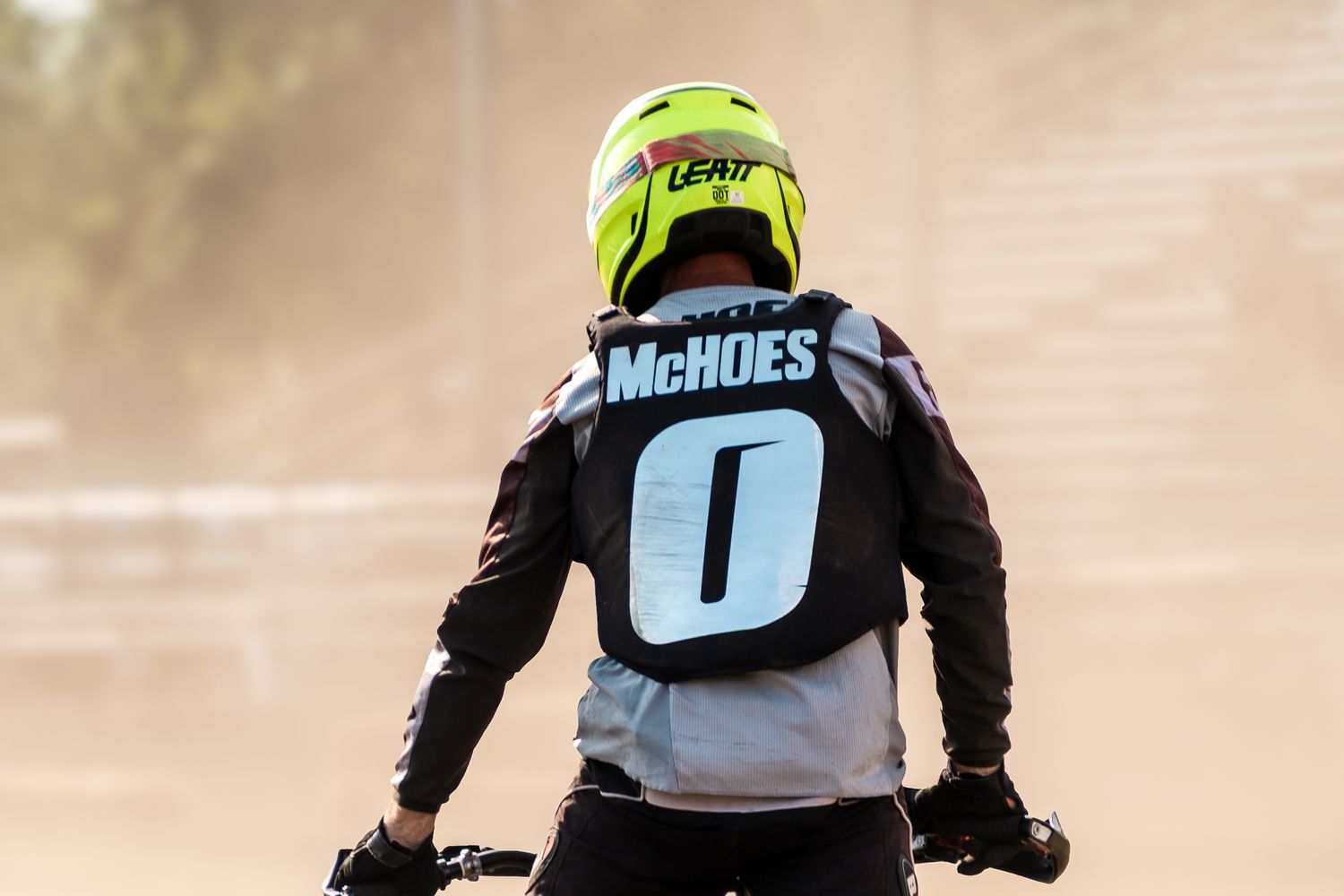 Motocross rider wearing number 0 McHoes jersey and yellow Leatt helmet on a dirt bike in dusty conditions.