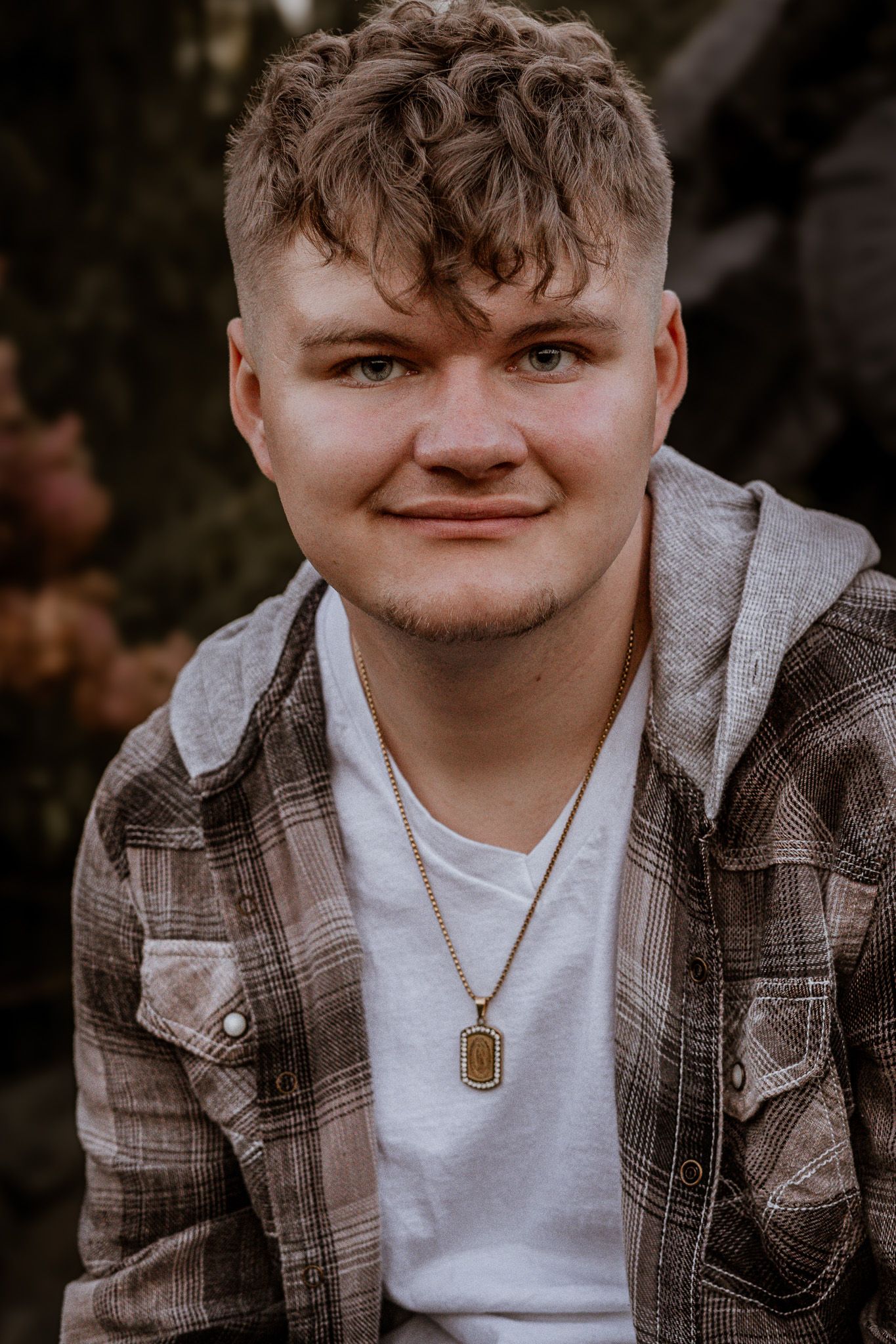 A person wearing a plaid jacket and white t-shirt smiles warmly at the camera.