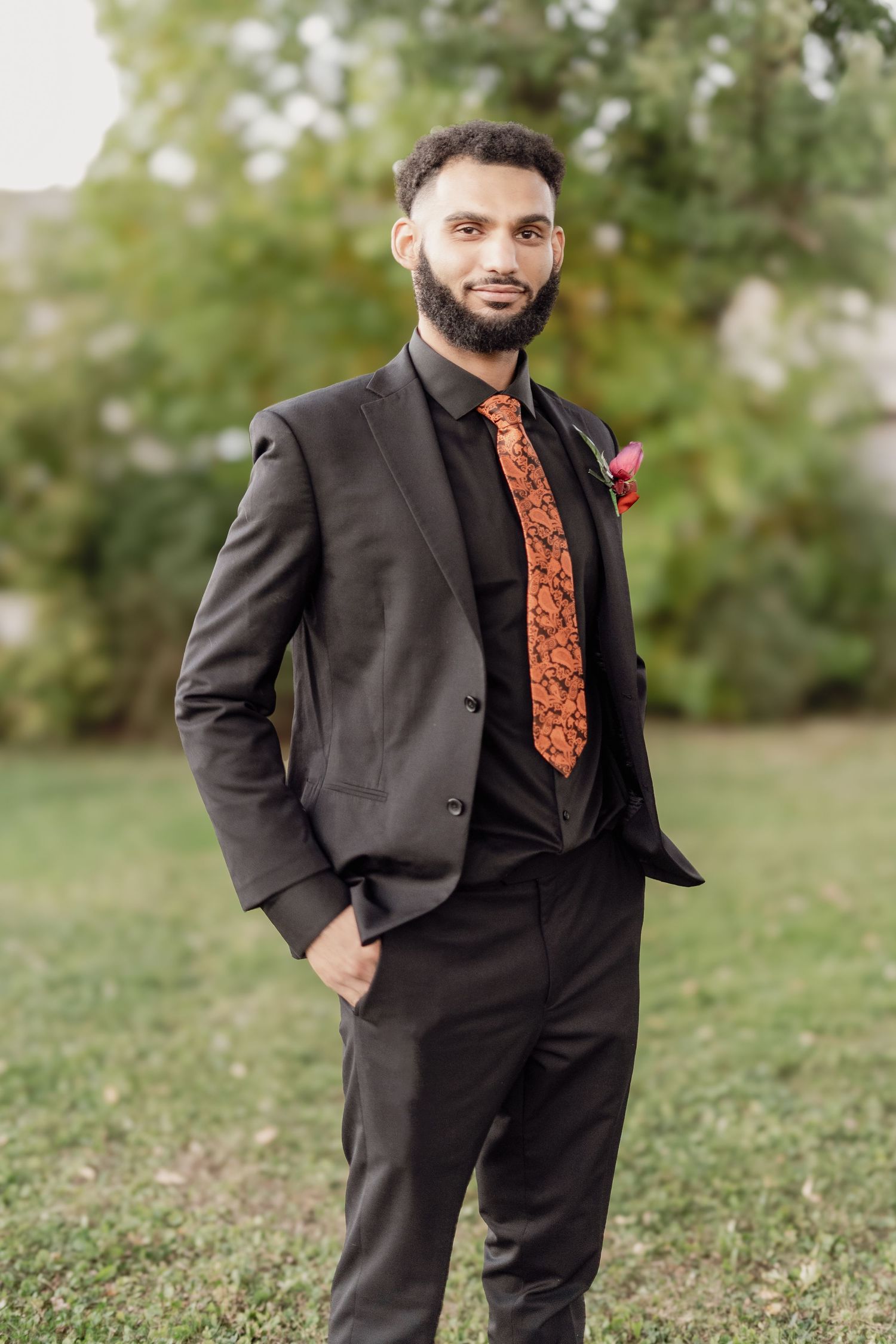 A person in a dark suit and orange patterned tie poses outdoors on grass in a series of similar shots.