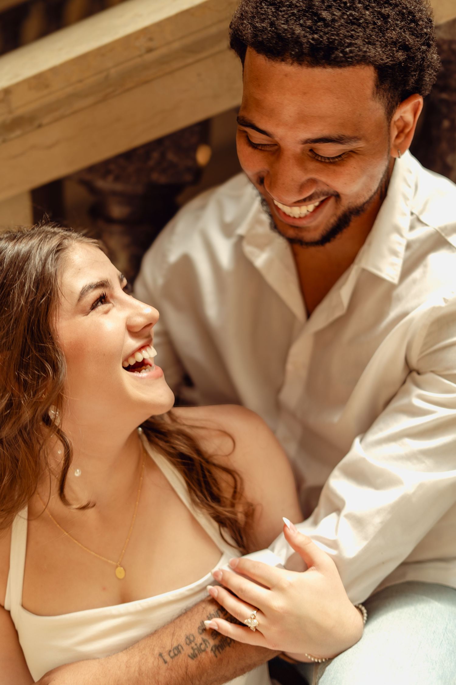 A joyful interracial couple laughing and sharing a tender moment together, dressed in white outfits.