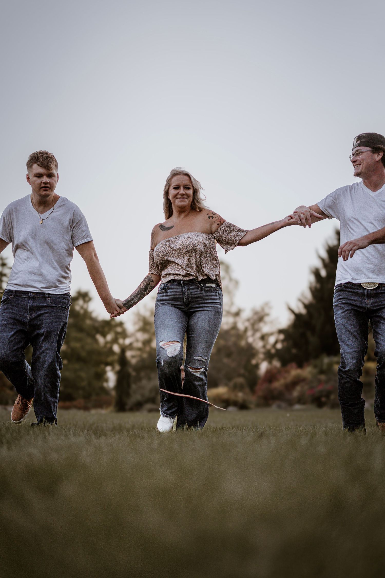 Three people holding hands while running through a grassy field at sunset.