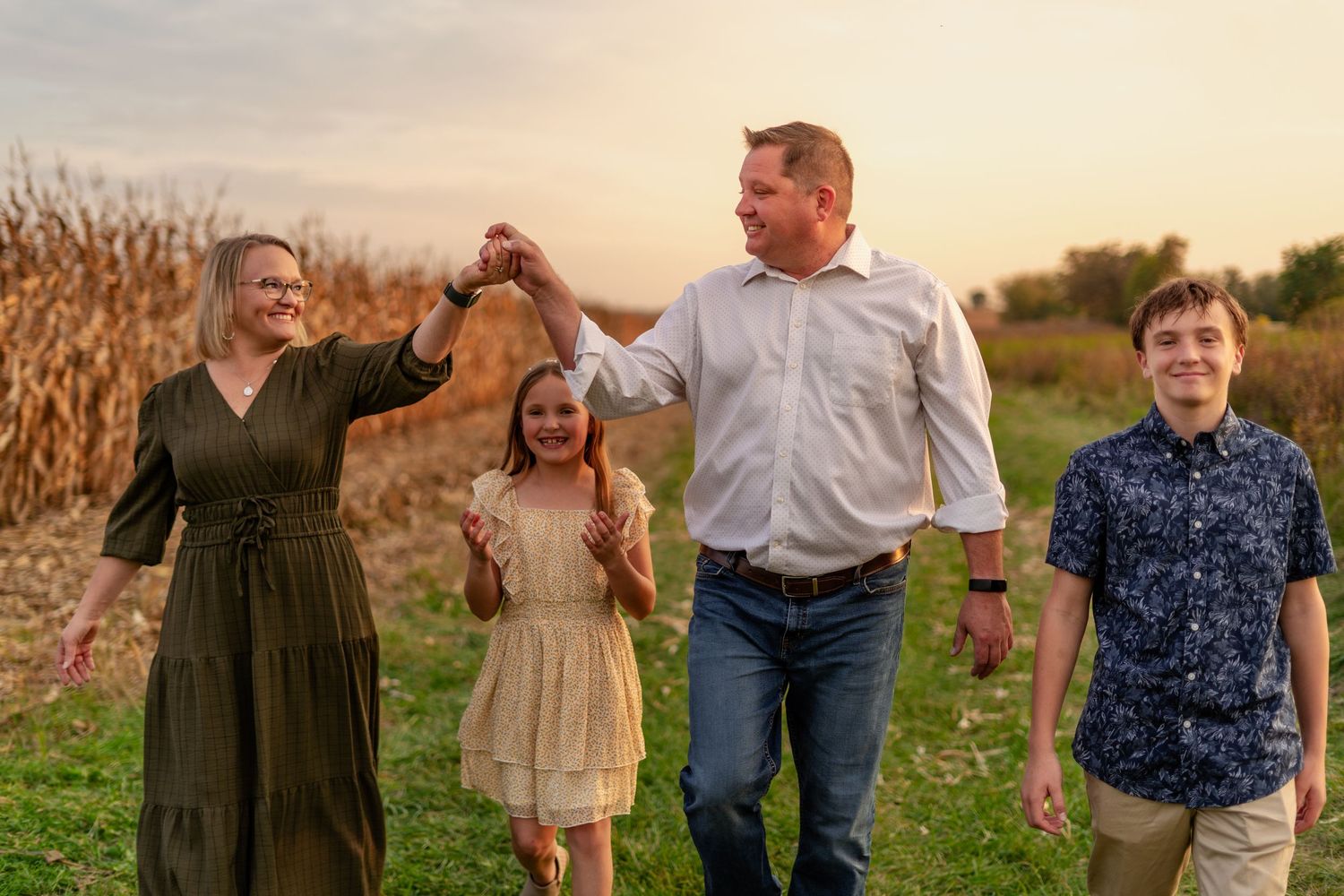 Family holding hands and walking together in a field during golden hour.