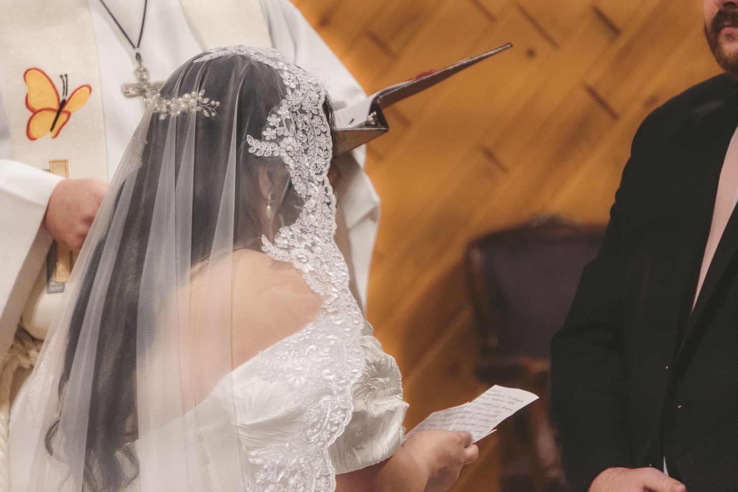 Bride in white lace wedding dress and veil stands at church altar during wedding ceremony.