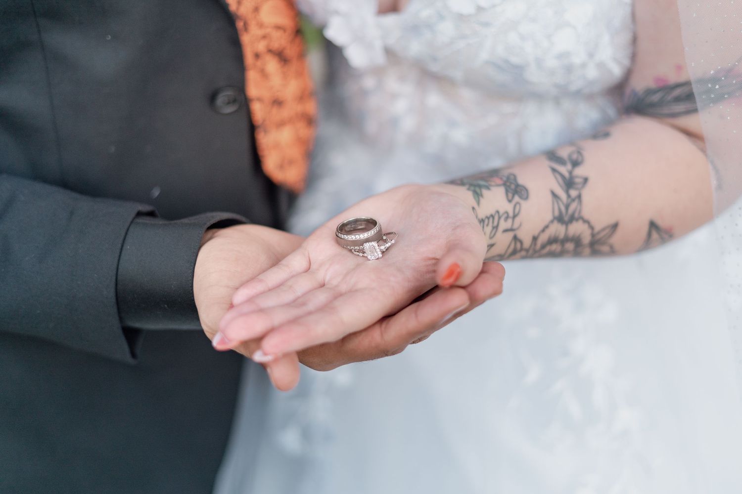 Close-up details of hands with wedding rings and tattoos.