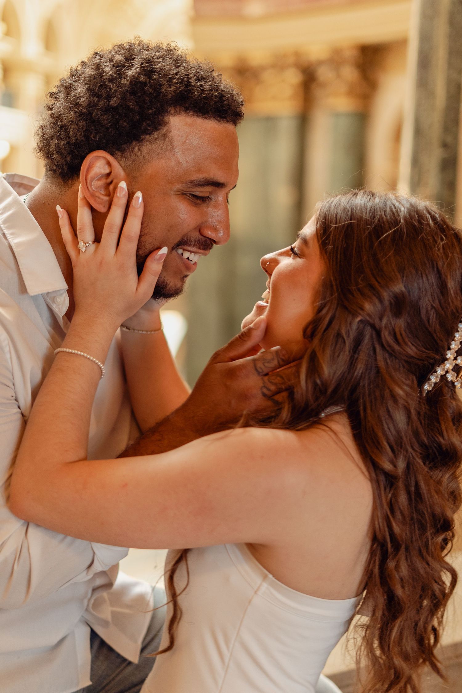 A joyful couple shares a romantic moment, smiling at each other, the bride in white with floral hair accessories.