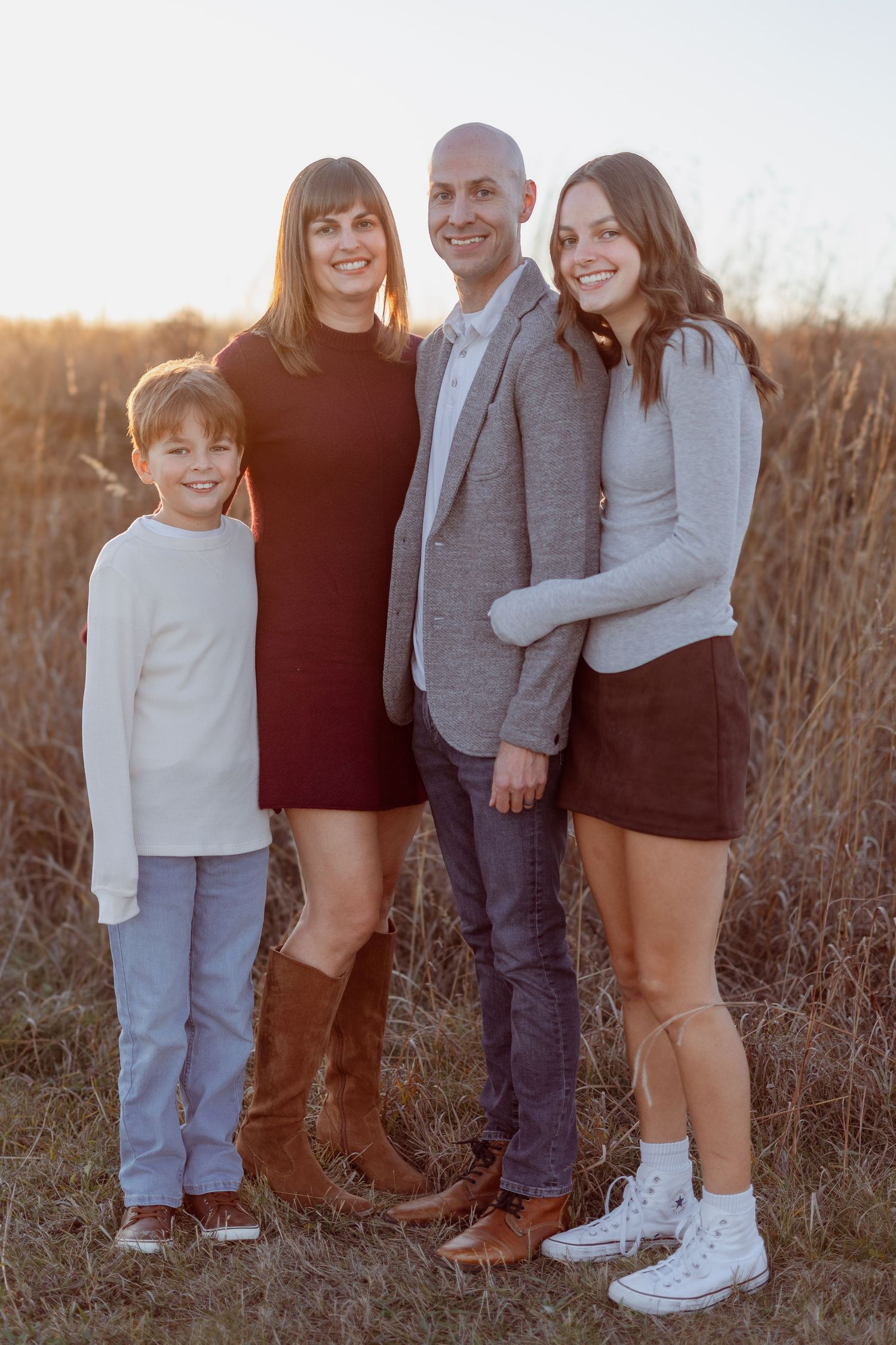 Family of four posing outdoors in a golden field during sunset, dressed in smart casual autumn attire.