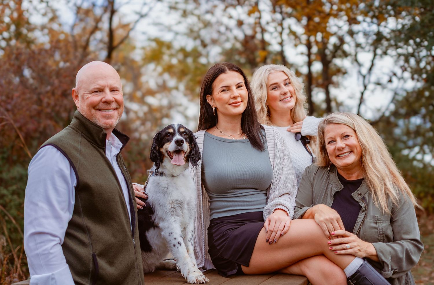 Family group with adult children daughters sitting outdoors with their dog during autumn photo session.