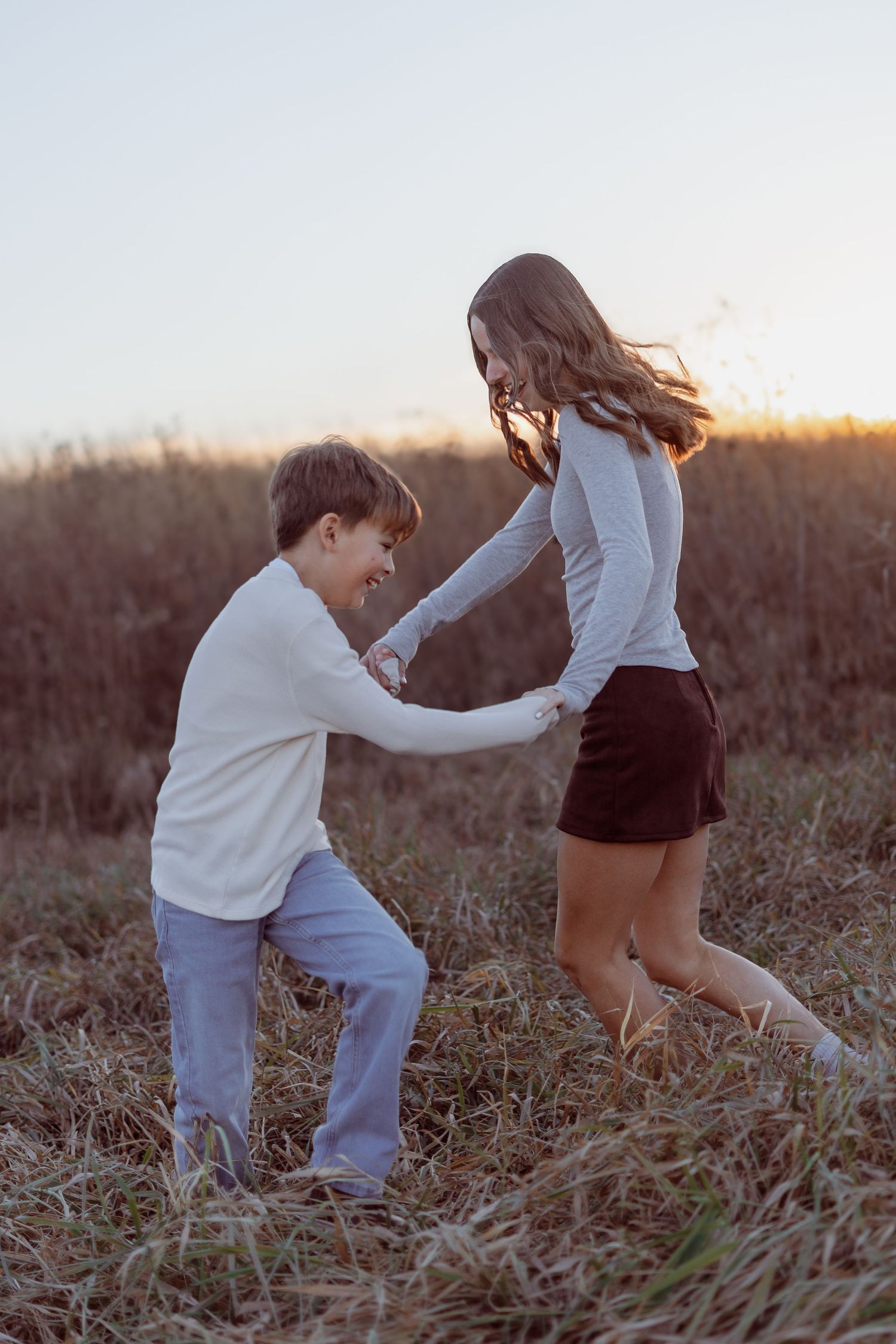 Two children playing and holding hands in a golden field at sunset, wearing casual white tops.
