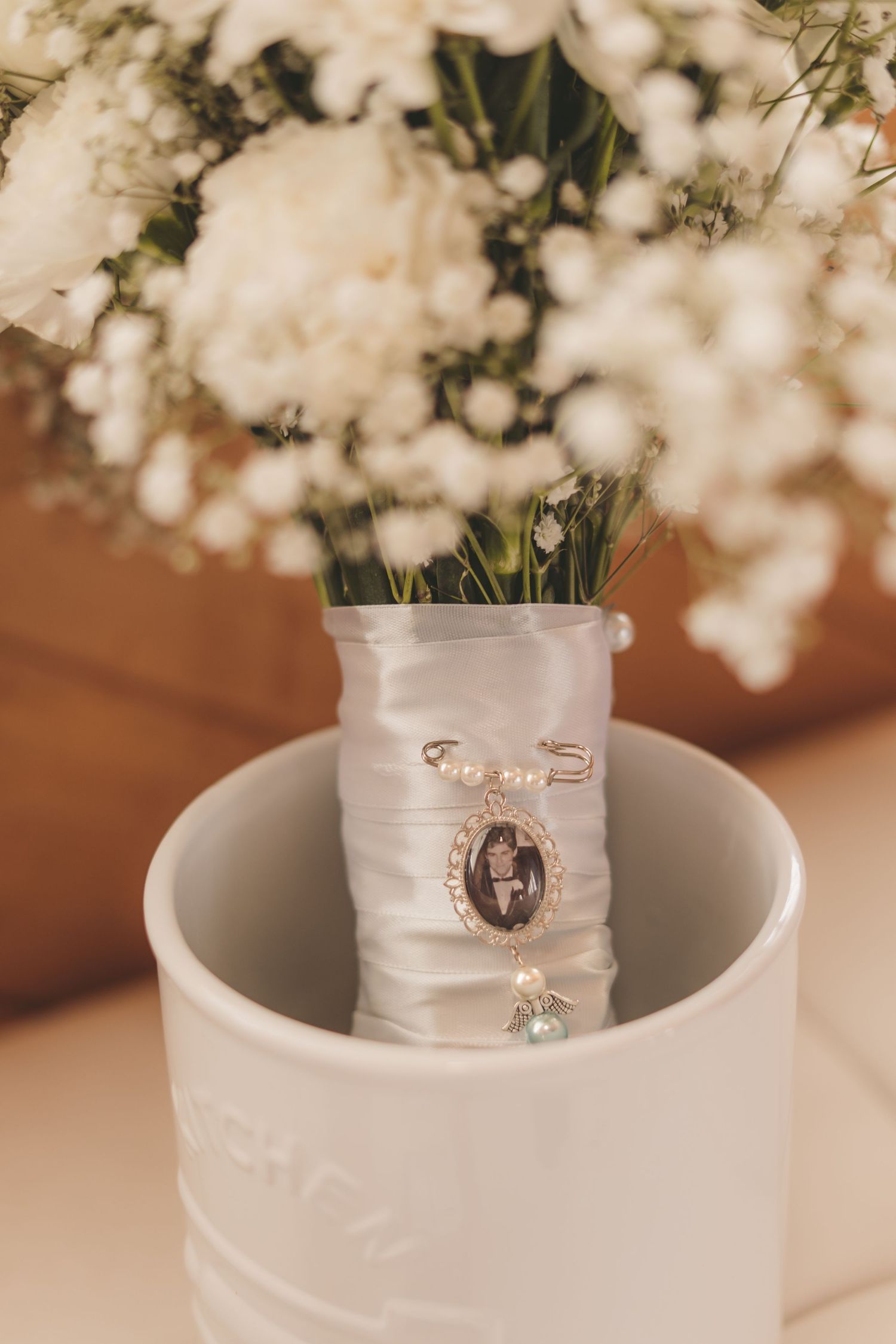 Wedding bouquet with white roses and baby's breath, adorned with a satin ribbon and vintage photo charm memorial pin.