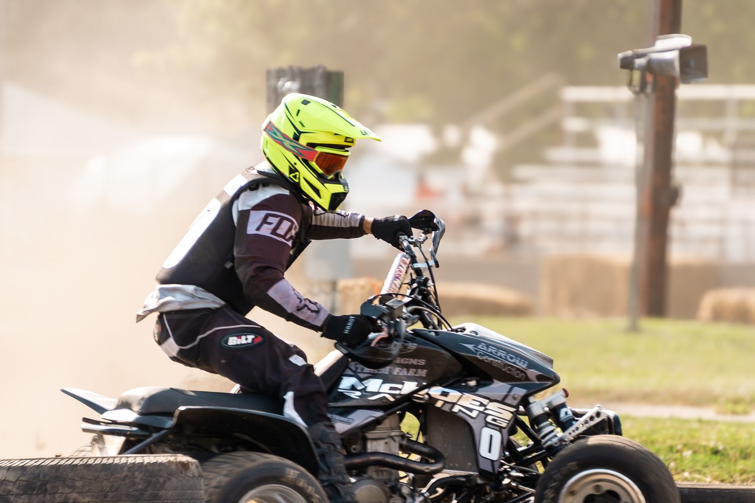 Rider in yellow helmet and black gear races a black ATV quad bike on a dirt track, kicking up dust.
