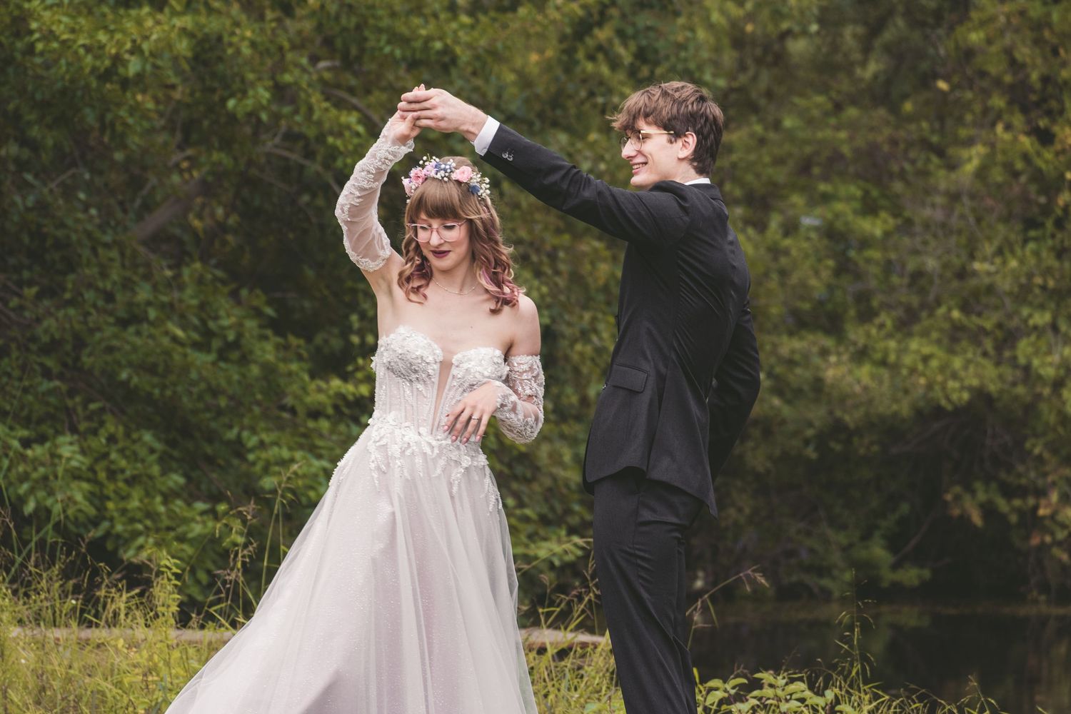 Bride and groom dancing outdoors in nature, wearing elegant wedding attire.