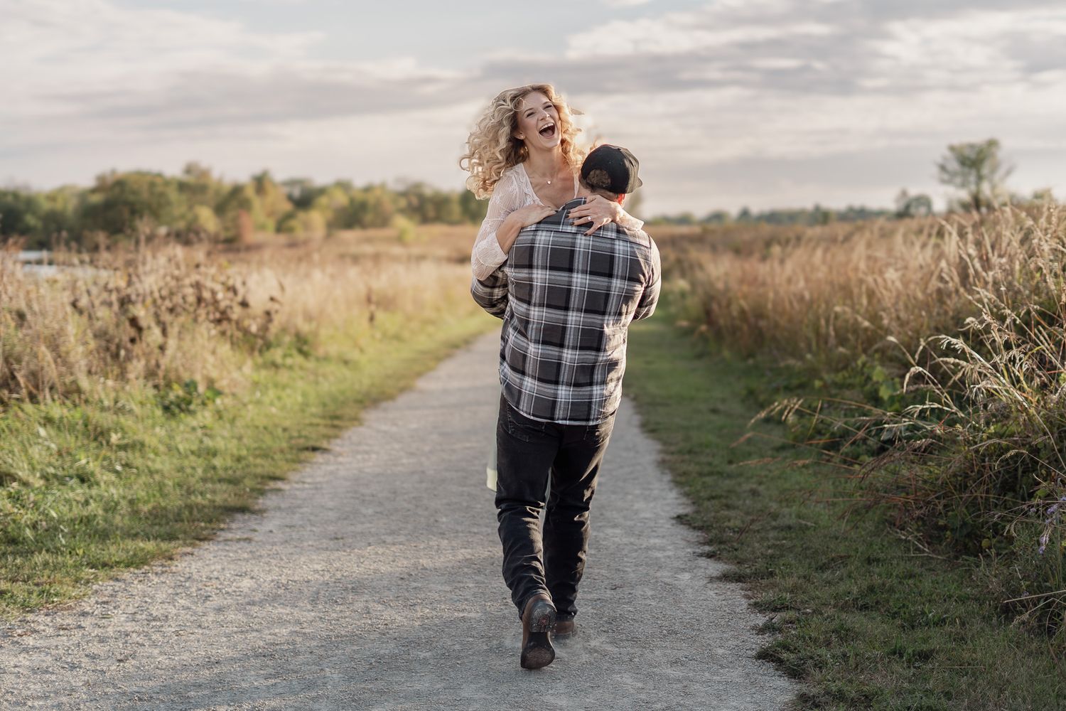 A couple walks together on a winding dirt path surrounded by autumn foliage.