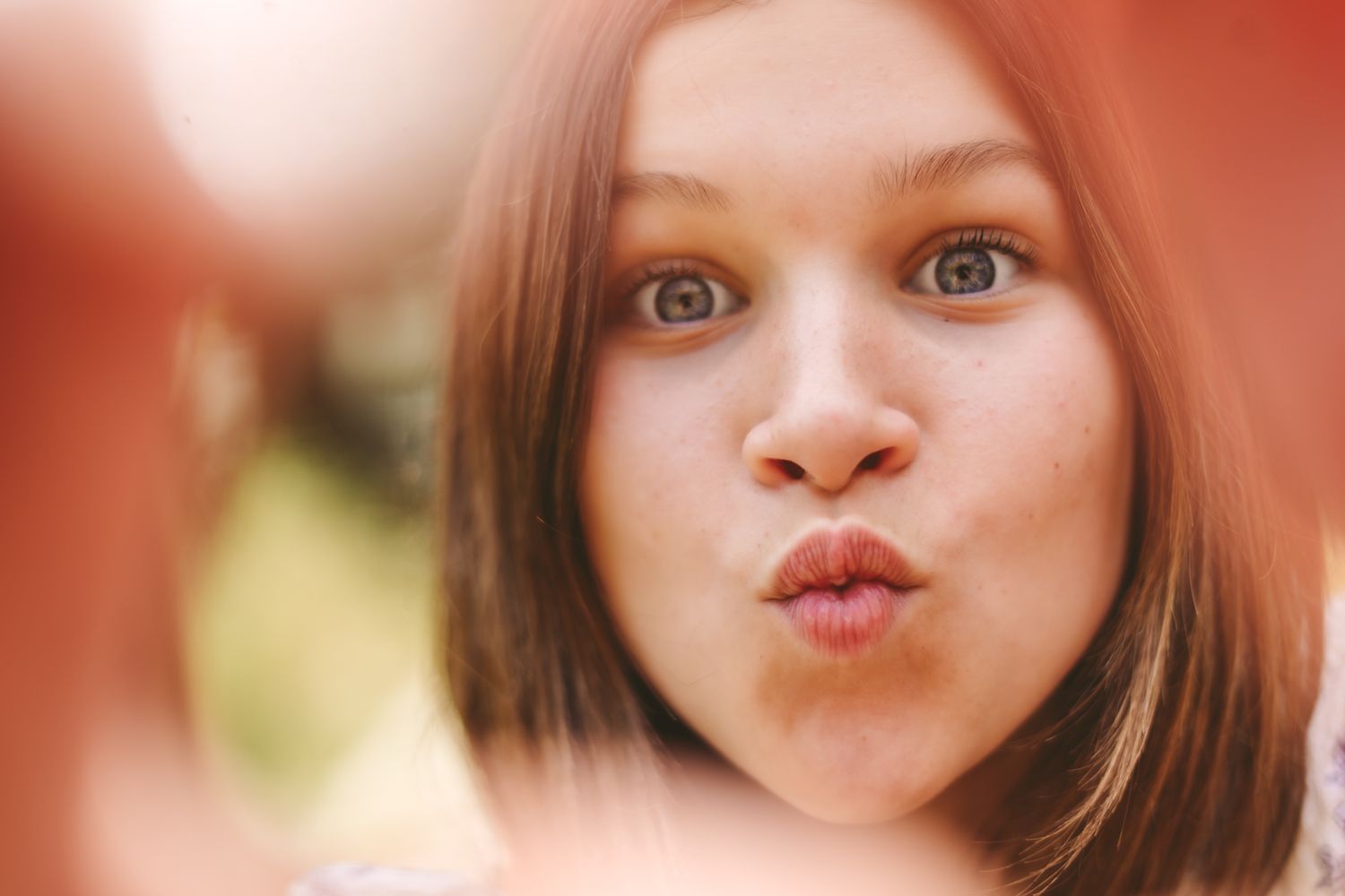 Young girl with freckles making a kissy face, close-up portrait with soft red bokeh background.