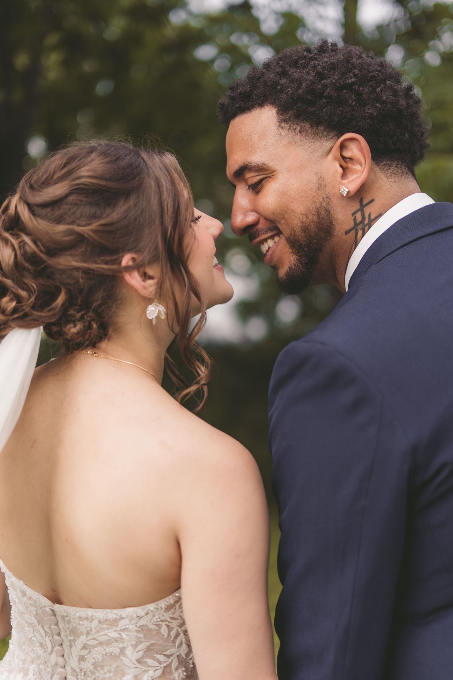 Bride and groom share a romantic moment, smiling at each other outdoors in wedding attire.