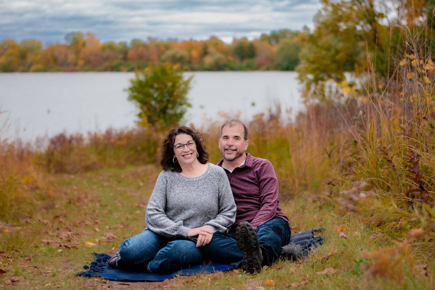 Couple relaxing together in an autumn field with cloudy skies.