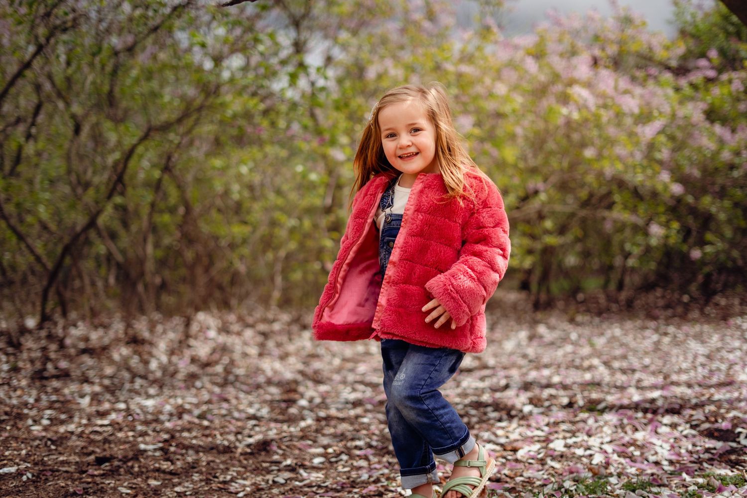 Child playing outdoors in autumn wearing a red jacket and jeans among fallen leaves.