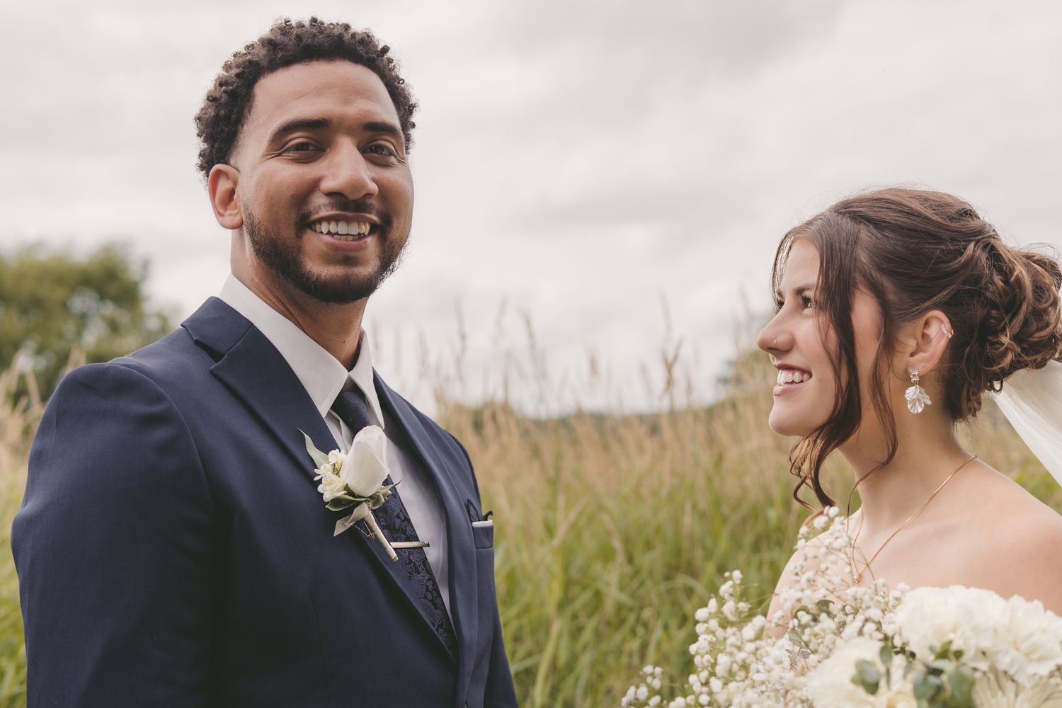 Happy bride and groom smiling outdoors on their wedding day in a field with tall grass.