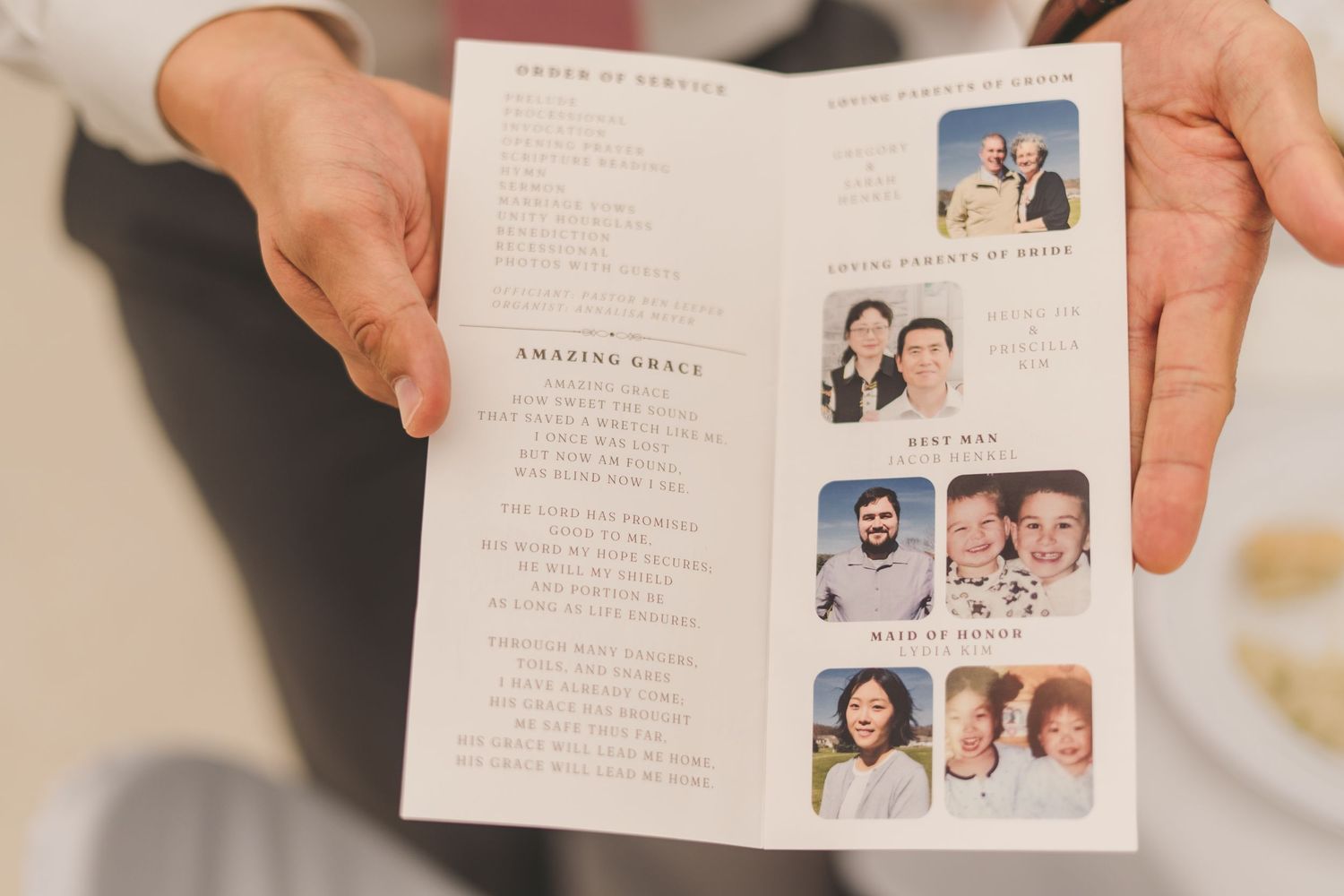 Hands holding a wedding program booklet featuring Amazing Grace lyrics and bridal party photos on the right side.