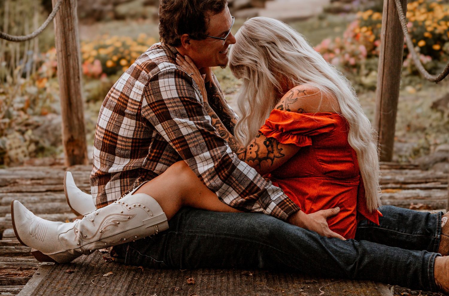 Intimate couple sitting on wooden deck wearing plaid and red during autumn photoshoot.