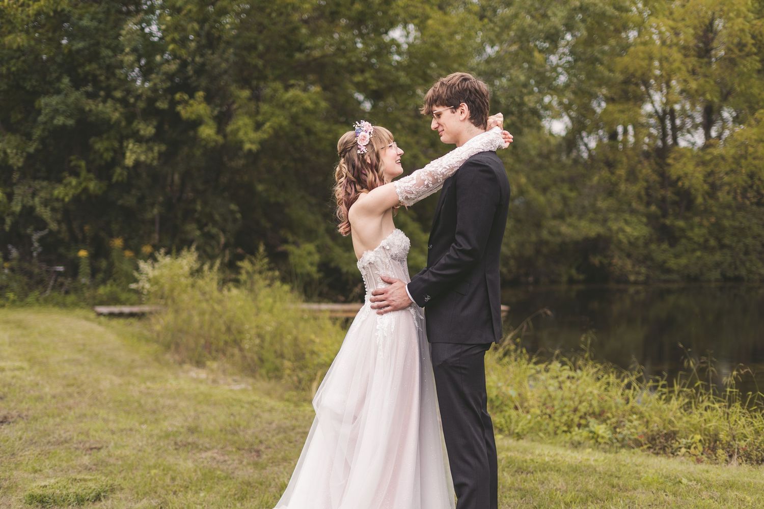 A newlywed couple embraces tenderly in a lush green outdoor setting on their wedding day.