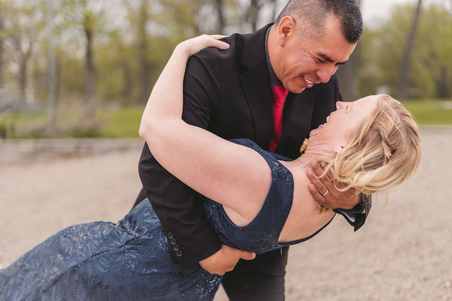 Couple dancing romantically outdoors, man in black suit with red tie dipping blonde woman in blue lace dress.