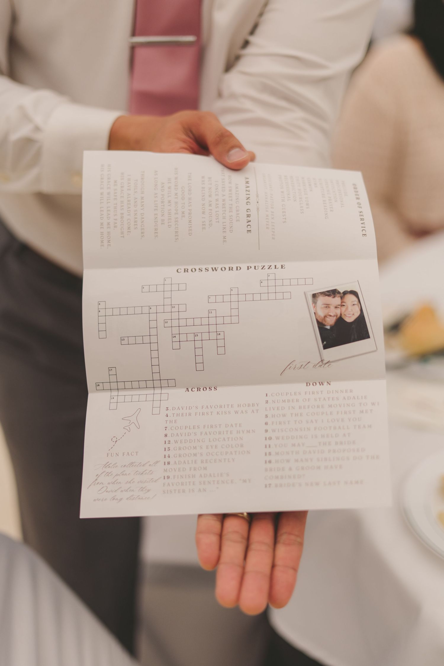 A person holds a wedding crossword puzzle program featuring a couples photo and clues about their relationship.