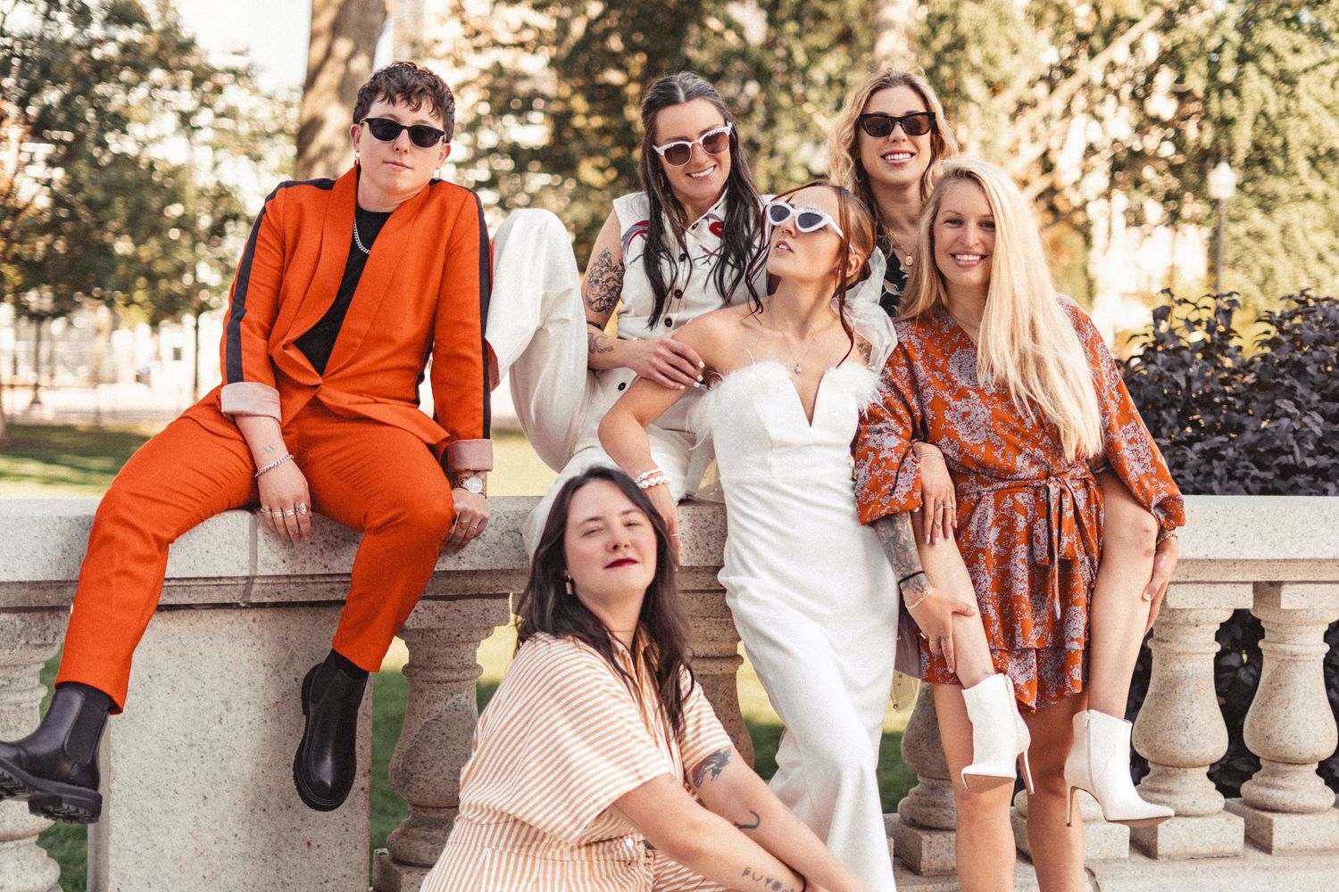 A group of friends in stylish summer outfits pose together on stone steps during a sunny afternoon.