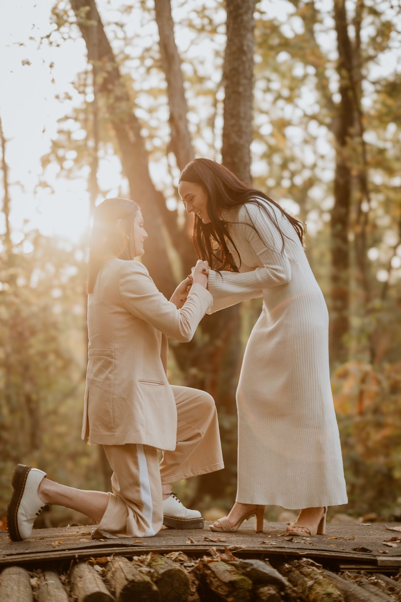 A couple shares a tender moment on a fallen tree trunk in a sunlit autumn forest.