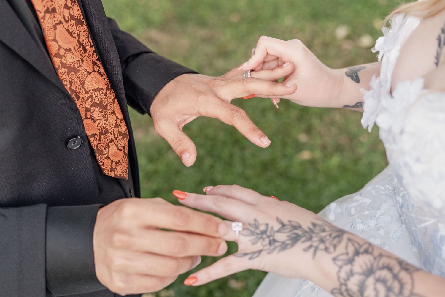 Close-up of hands placing wedding bands during a ceremony against a natural outdoor setting.