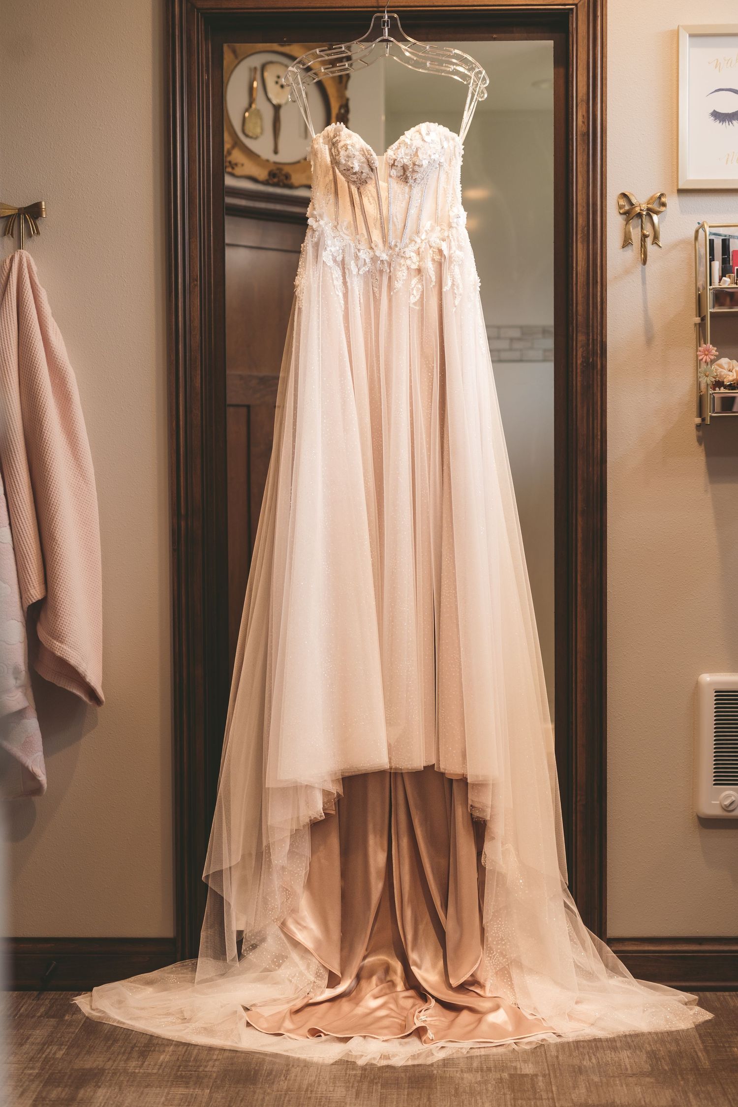Elegant blush tulle wedding gown with floral bodice displayed on hanger in a warmly lit dressing room.
