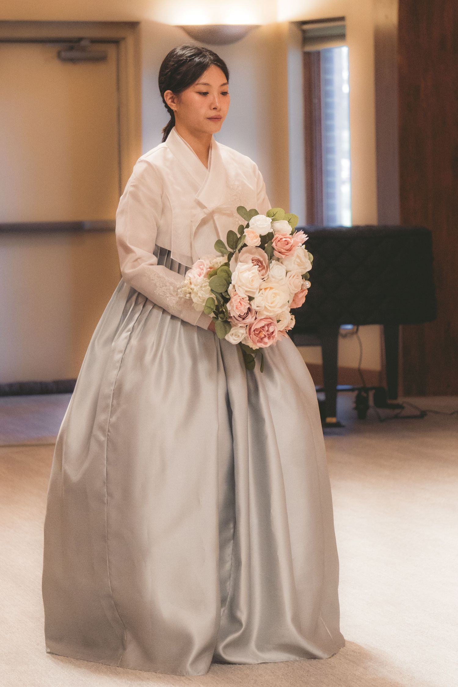Woman in traditional Korean hanbok wedding dress holding a bouquet of pink and white roses.