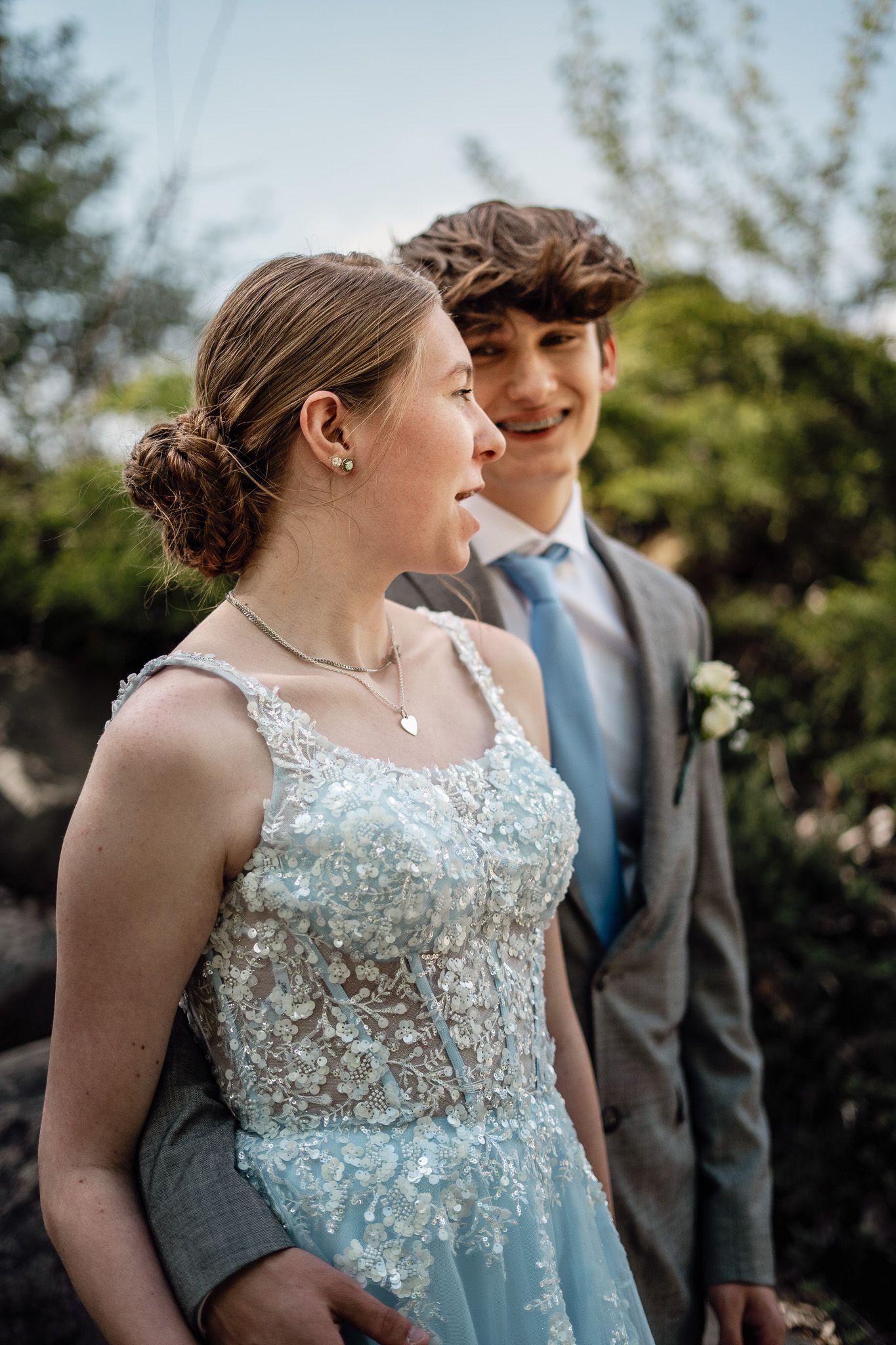 A joyful prom couple in formal attire share a candid moment outdoors.