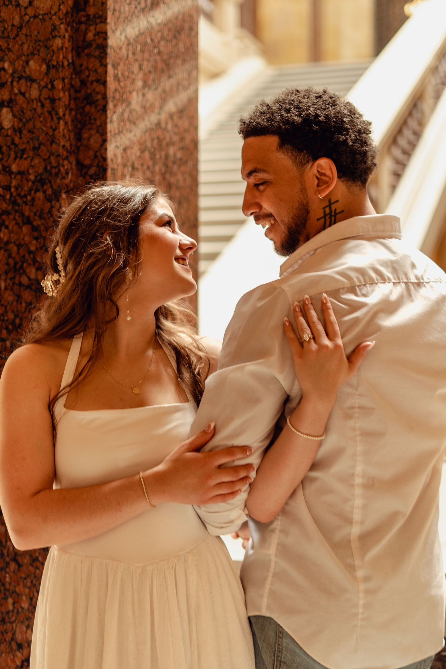 Joyful interracial couple embracing and laughing together near ornate stone columns in sunlight.