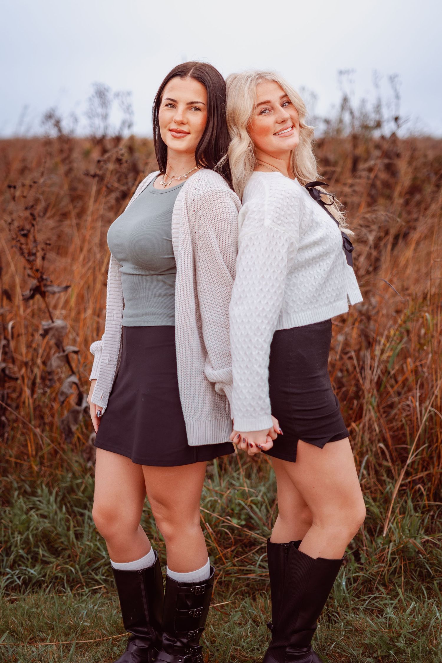 Two friends in matching outfits pose back-to-back in autumn field.